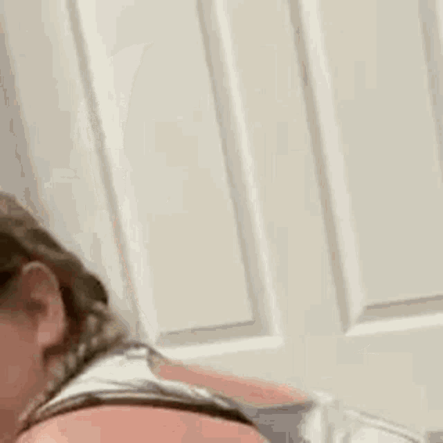 a woman wearing glasses and a braid is sitting in front of a white door .