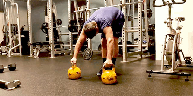 a man in a purple shirt is lifting a kettlebell in a gym