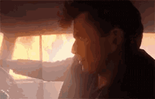 a man is sitting in the driver 's seat of a car with a fire in the background .