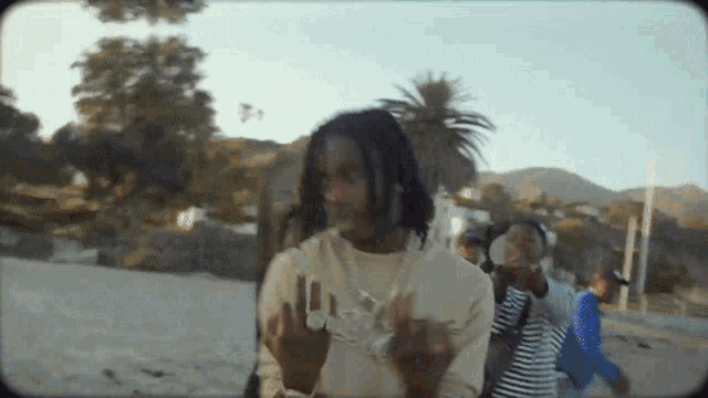 a man with dreadlocks is standing on a beach giving the middle finger .