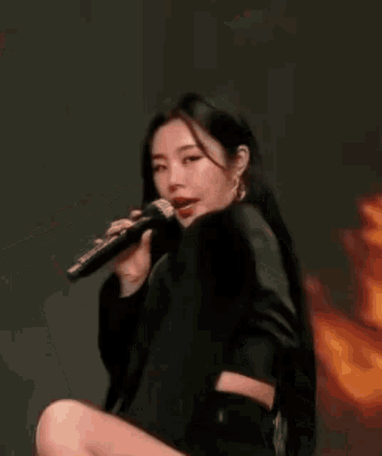 a woman is kneeling down while holding a microphone in front of a fire background .