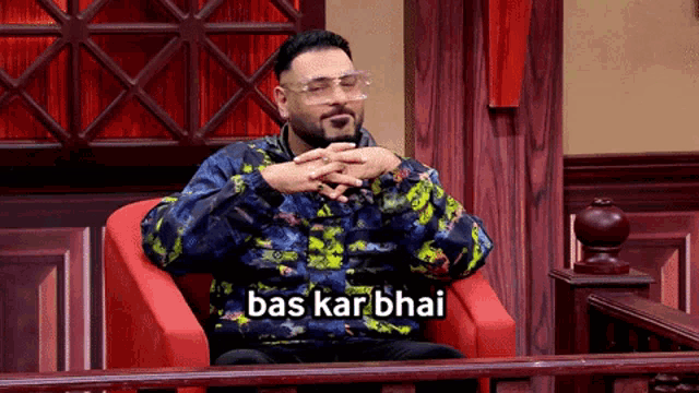 a man wearing glasses is sitting in a chair with bas kar bhai written on the bottom
