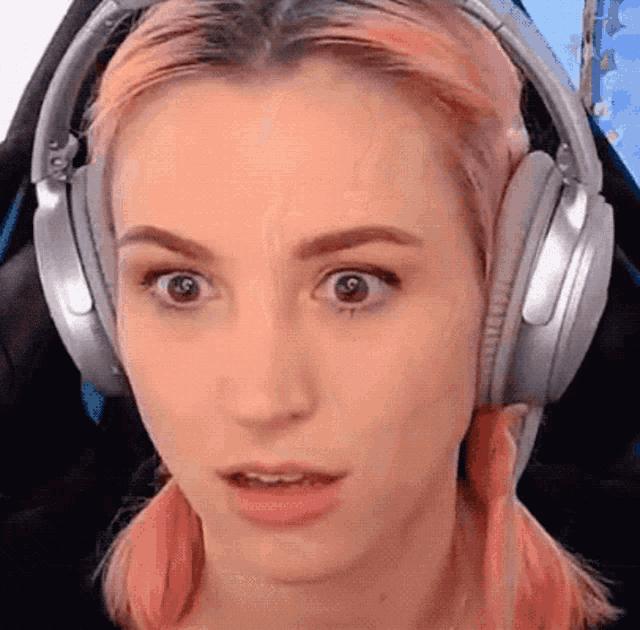 a woman with pink hair is wearing headphones and looking at the camera .