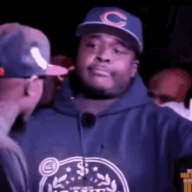 a man wearing a hat with the letter c on it is talking to another man .