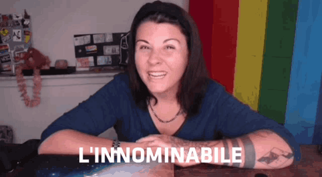 a woman sitting in front of a rainbow flag with l' innominabile written on her arm