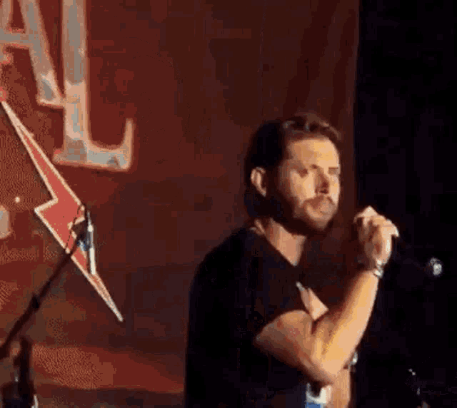 a man is singing into a microphone on a stage in front of a red lightning bolt .