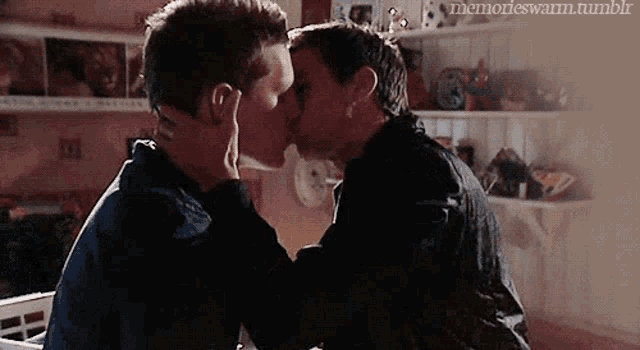 a couple of men are kissing in a room .