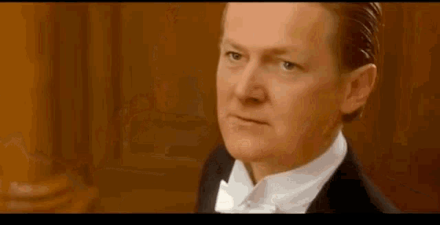 a man in a tuxedo and bow tie is looking at the camera and making a serious face .