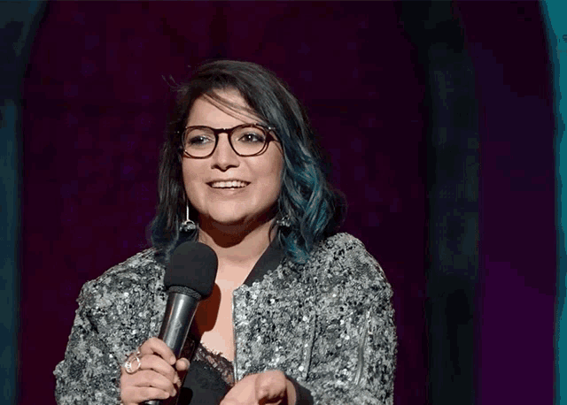 a woman with glasses and blue hair holds a microphone