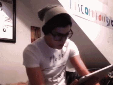 a man wearing glasses and a beanie is using a tablet in front of a sign that says icon