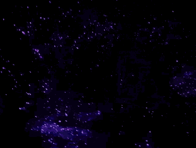 purple and blue lights are flying through the air in a dark room