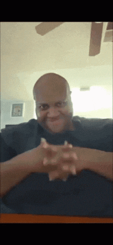 a bald man is sitting at a table with his hands folded in front of his face