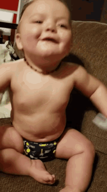 a baby in a diaper is sitting on a couch smiling