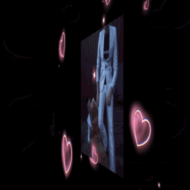 a man in a white suit is standing next to another man in a black shirt surrounded by pink hearts .