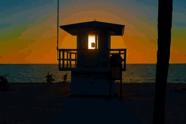 a lifeguard tower on a beach at sunset with people walking on the beach .