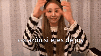 a woman in a striped sweater is making a heart with her hands and the words corazon si eres de joy .