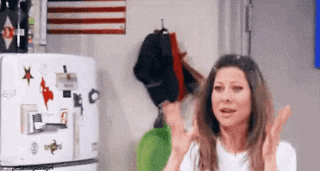 a woman is standing in front of a refrigerator with a hat hanging on it .