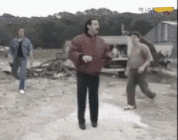 a man in a red jacket is dancing on a dirt road
