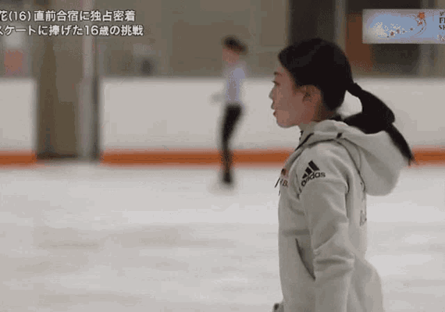 a woman wearing a white adidas jacket stands on a rink