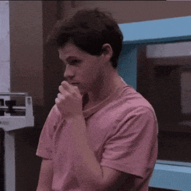 a young man wearing a pink shirt is covering his mouth with his hand
