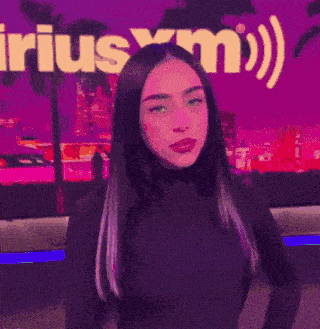 a woman in a black shirt is standing in front of a purple sign that says ' xm ' .