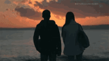 a man and a woman standing on a beach watching the sunset