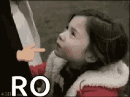 a little girl is pointing at a person 's face .