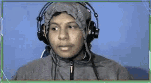 a man wearing headphones and a hood is smiling and pointing .