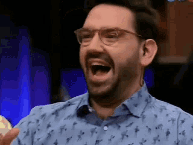 a man wearing glasses and a blue shirt is laughing with his mouth open .