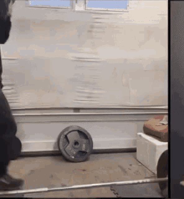 a man is lifting a barbell in a garage while a weight plate sits on the floor .
