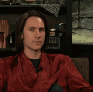 a man wearing a red robe is sitting in front of a bookshelf