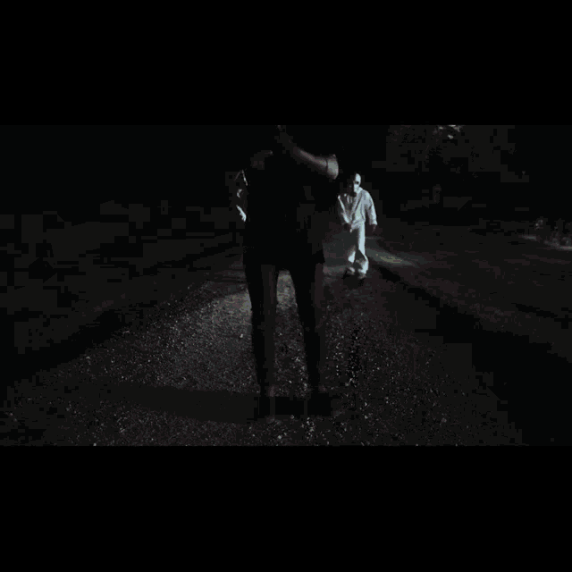 a man in a black shirt is standing in the dark with two people in white suits behind him
