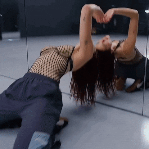 a woman is kneeling down in front of a mirror making a heart shape with her hands