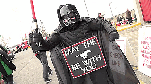 a man in a darth vader costume holding a sign that says may the be with you