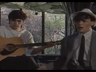 two men singing and playing guitars in front of a window