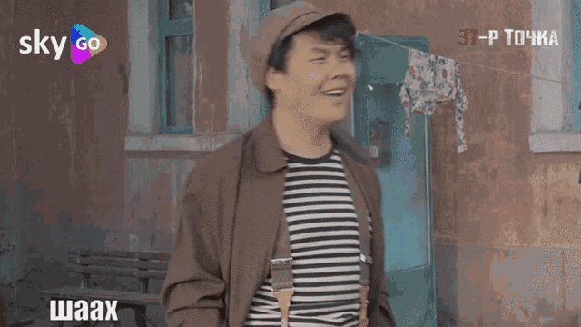 a man in a striped shirt is smiling in front of a sky go sign