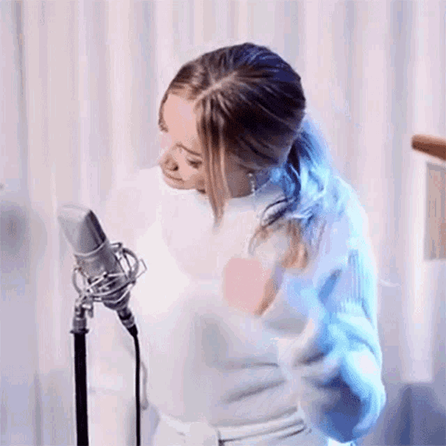a woman is standing in front of a microphone with her hands in her hair