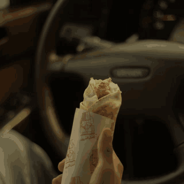 a person holding a sandwich in front of a steering wheel that says ford
