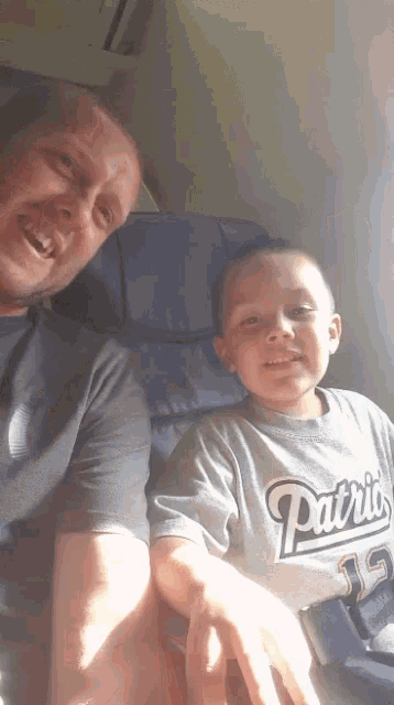 a boy wearing a patriots shirt sits next to his father