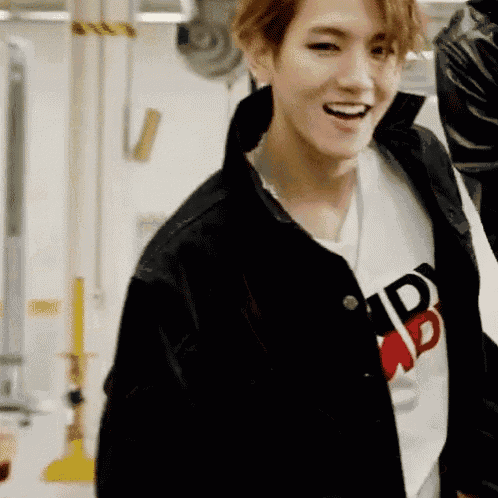 a young man wearing a black jacket and a white t-shirt with the letter b on it is smiling .