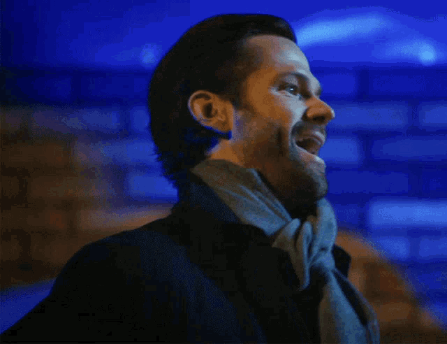 a man with a scarf around his neck smiles in front of a blue background