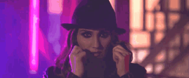 a woman wearing a hat is covering her face with her hand