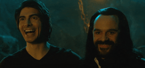 a man with a beard is smiling next to another man with long hair
