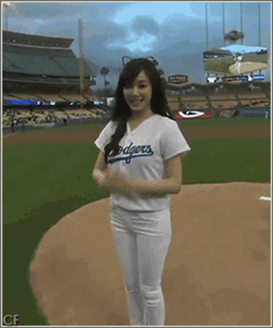 a woman wearing a dodgers jersey stands on the mound