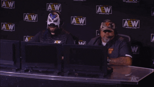 two men are sitting in front of a wall that says aew