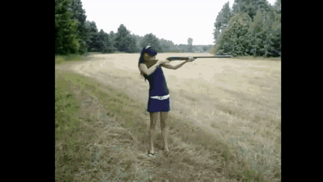 a woman in a blue dress is standing in a field holding a shotgun