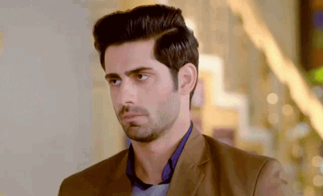 a man in a brown suit and blue shirt is looking at the camera