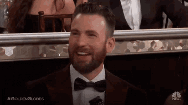 a man in a suit and bow tie is smiling while sitting in a row at a nbc event .