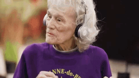an elderly woman wearing headphones and a purple shirt is running on a treadmill .