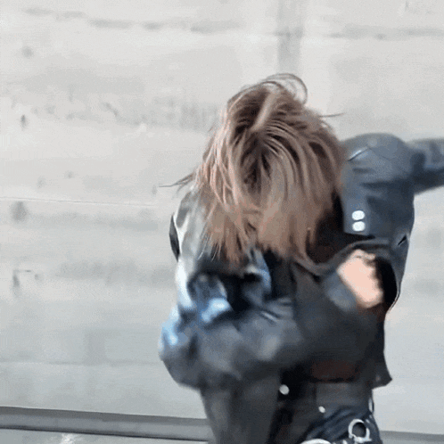a woman wearing a leather jacket is dancing in front of a wall